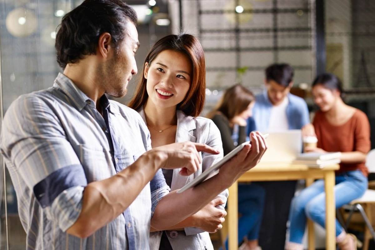 Two people are looking at a tablet in front of other people.