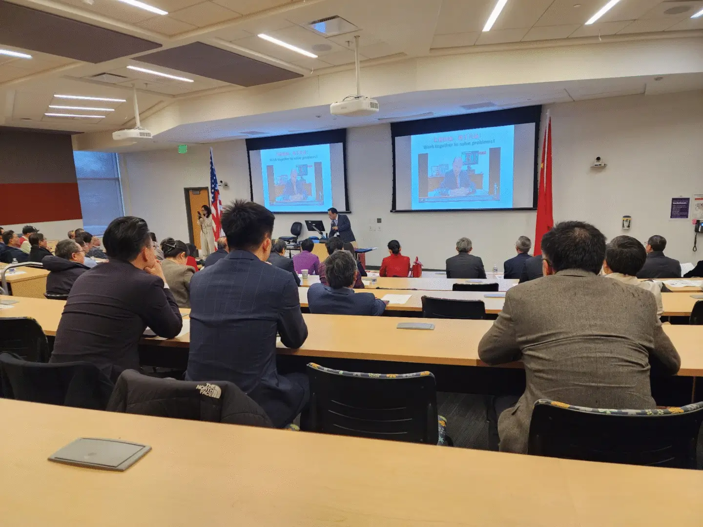Lecture hall with attendees and presentation screens.