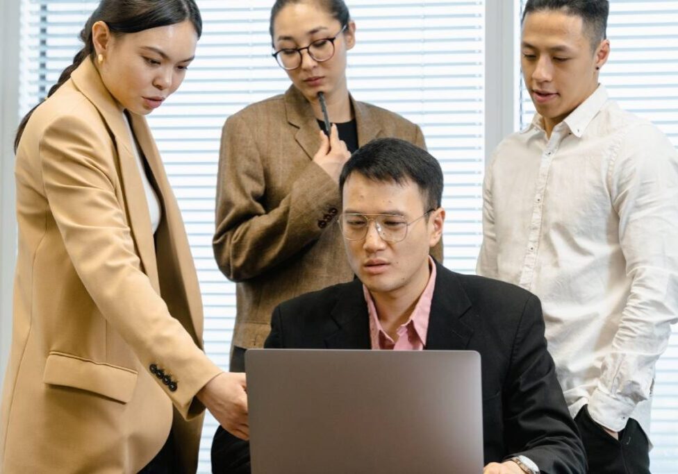 A group of people standing around a man on a laptop.